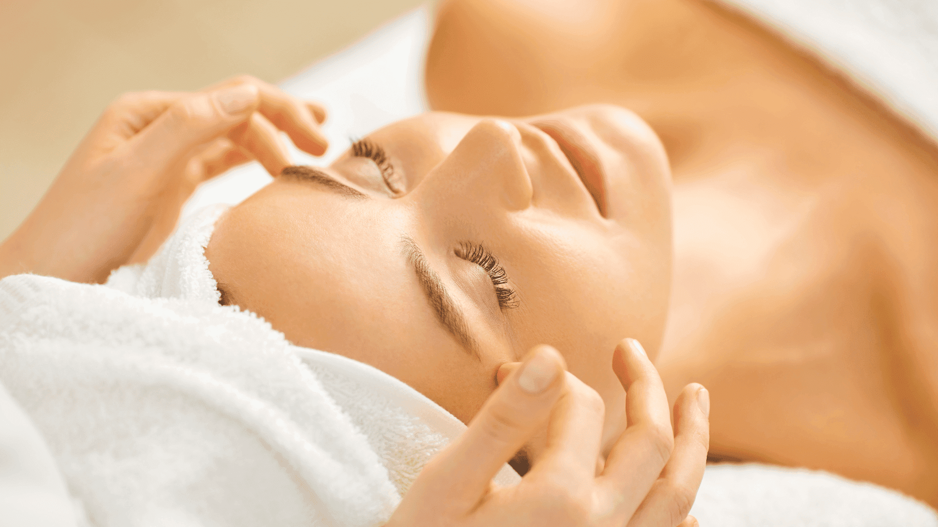 Woman receiving a relaxing facial massage with a towel around her head.