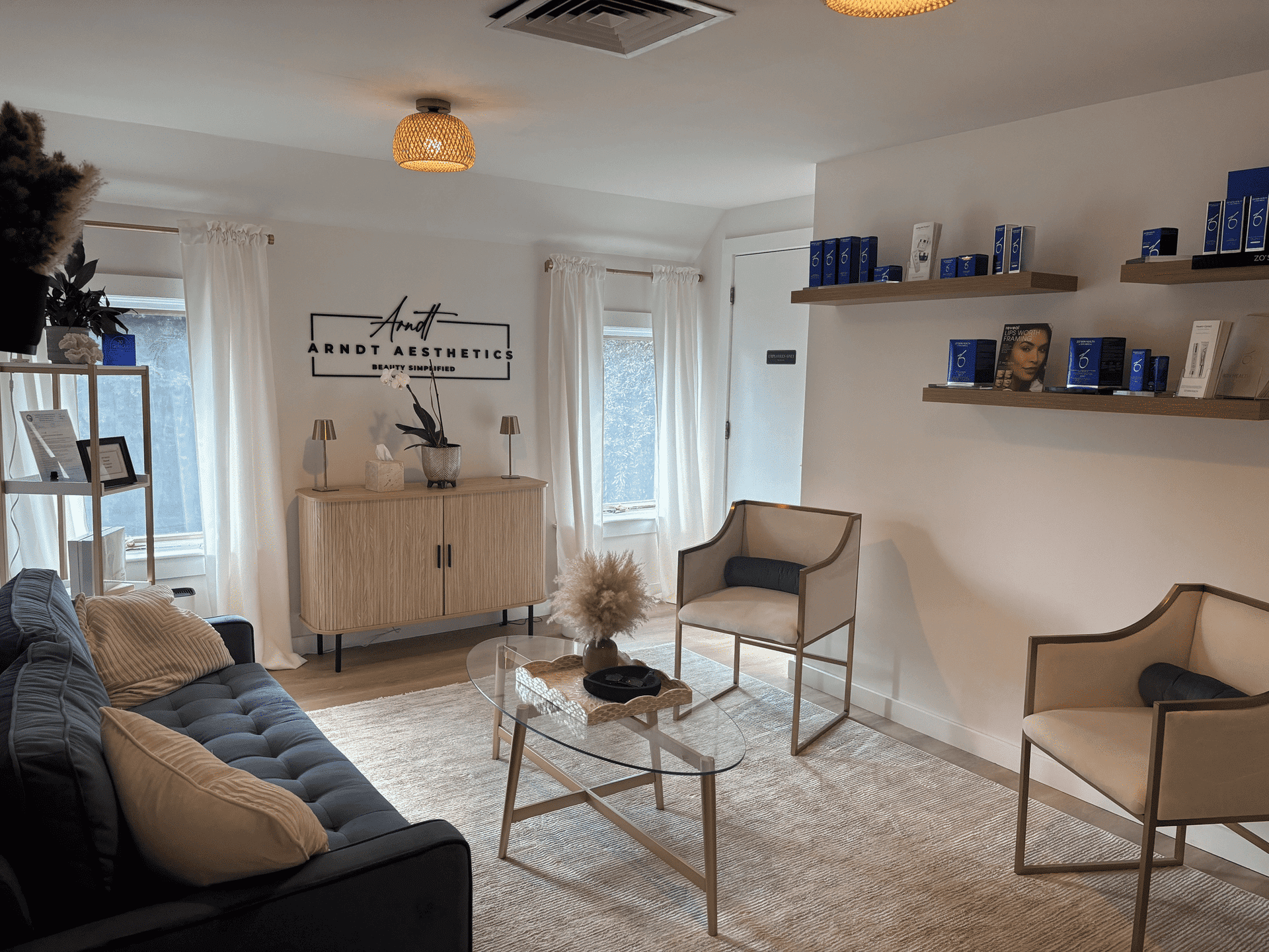 Cozy aesthetic clinic lounge with modern decor, seating, and skincare products on shelves.